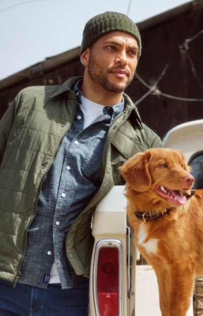 Person wearing a knit cap leaning on a pickup truck beside a golden retriever dog outdoors.