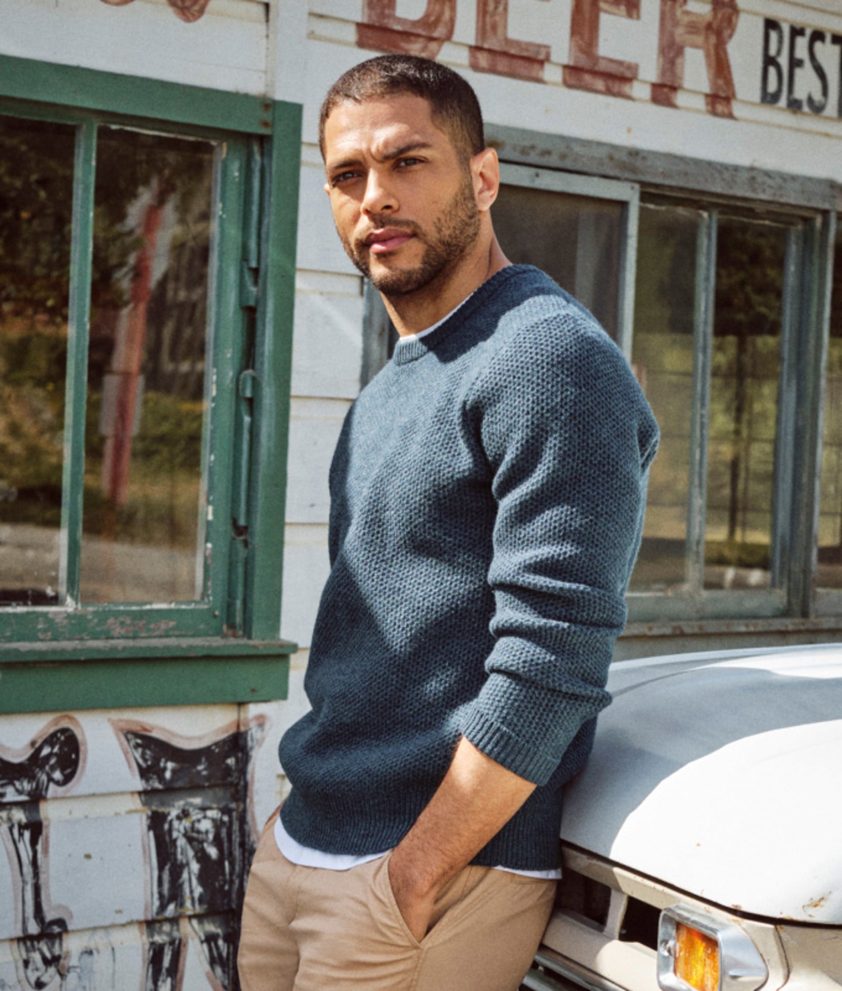 Man in a blue crewneck sweater standing beside a vintage storefront. 