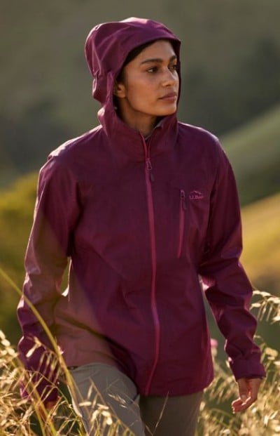 Person in a burgundy hooded rain jacket standing in a grassy field.
