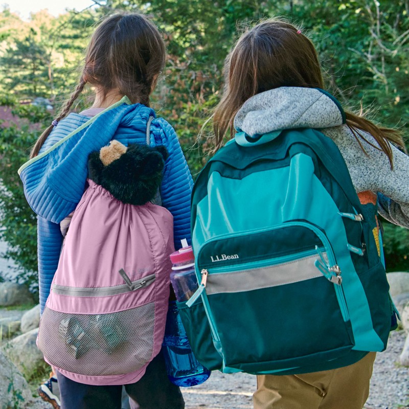 2 girls from behind walking on a wooded path wearing backpacks.