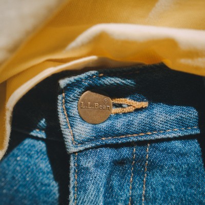 A close-up of an L.L.Bean brass button on jeans, a yellow shirt tucked in above it.