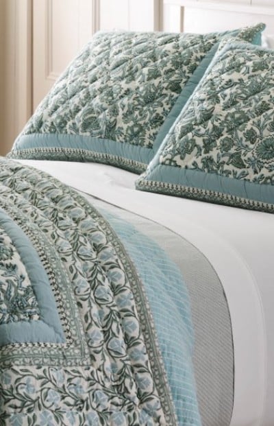 Textured blue and sage quilted bedding with decorative trim layered across a neatly made bed.