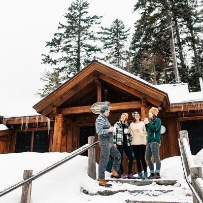 A woman outside on snowshoes, arm outstretched above a dog standing on hind legs.