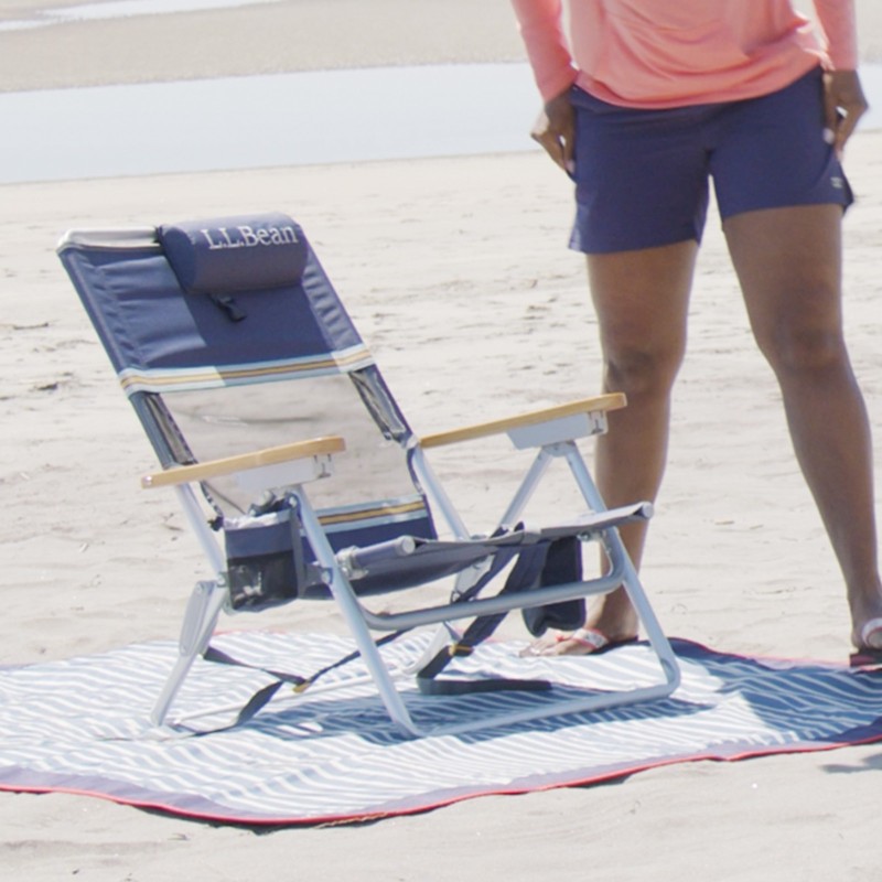 A foldable beach chair set up on a beach blanket on the sand.