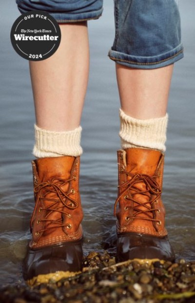 Close up of a person in L. L. Bean boots and jeans standing shallow water along a rocky shoreline.