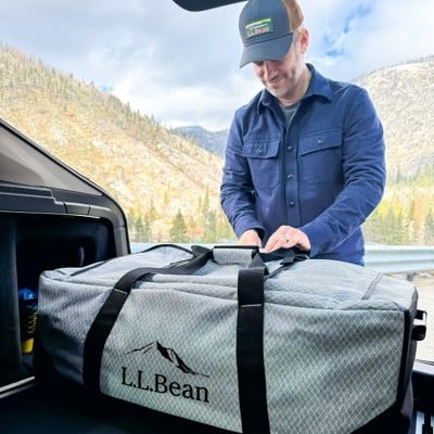 Man fastening a large L. L. Bean duffle in the back of a vehicle.