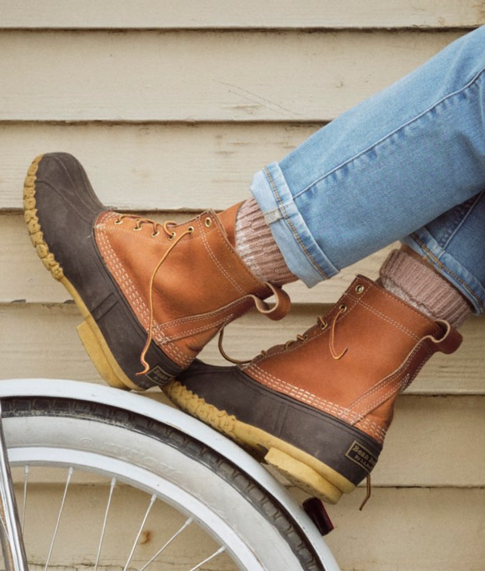 A pair of brown ankle high L L Bean Boots casually resting on bicycle fender.