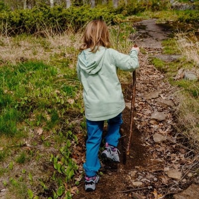 A shot from behind of a young girl walking on a path with a walking stick.