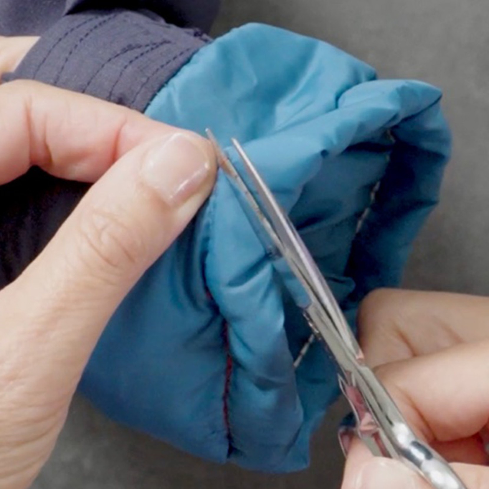 Hands use small scissors to cut a thread on the cuff of a blue and navy jacket sleeve