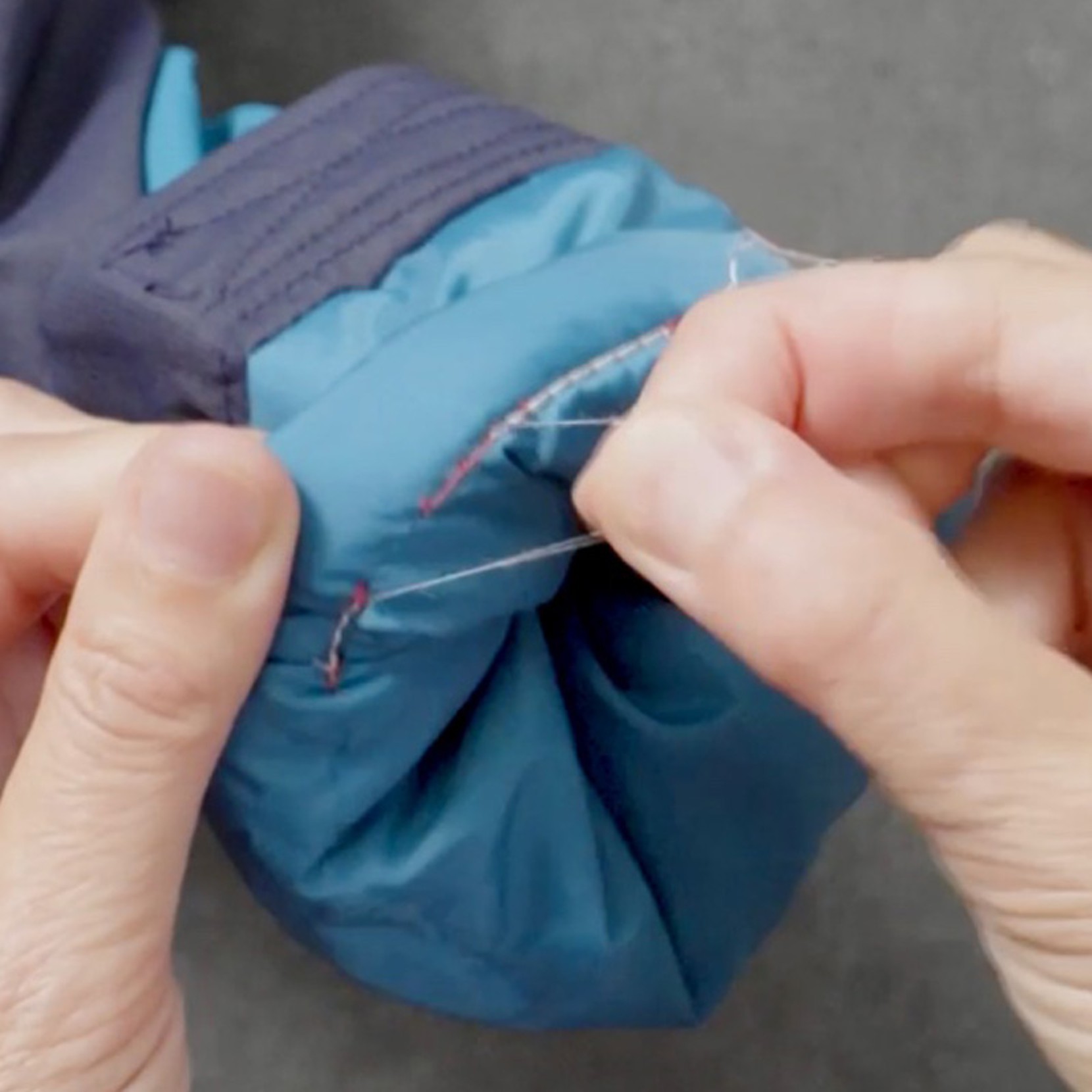 Hands hold a blue jacket sleeve and use scissors to cut a loose thread.